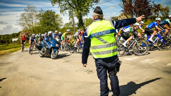 Gendarme équipé d'un chasuble jaune gendarmerie, de dos, indiquant le sens de la course aux cyclistes